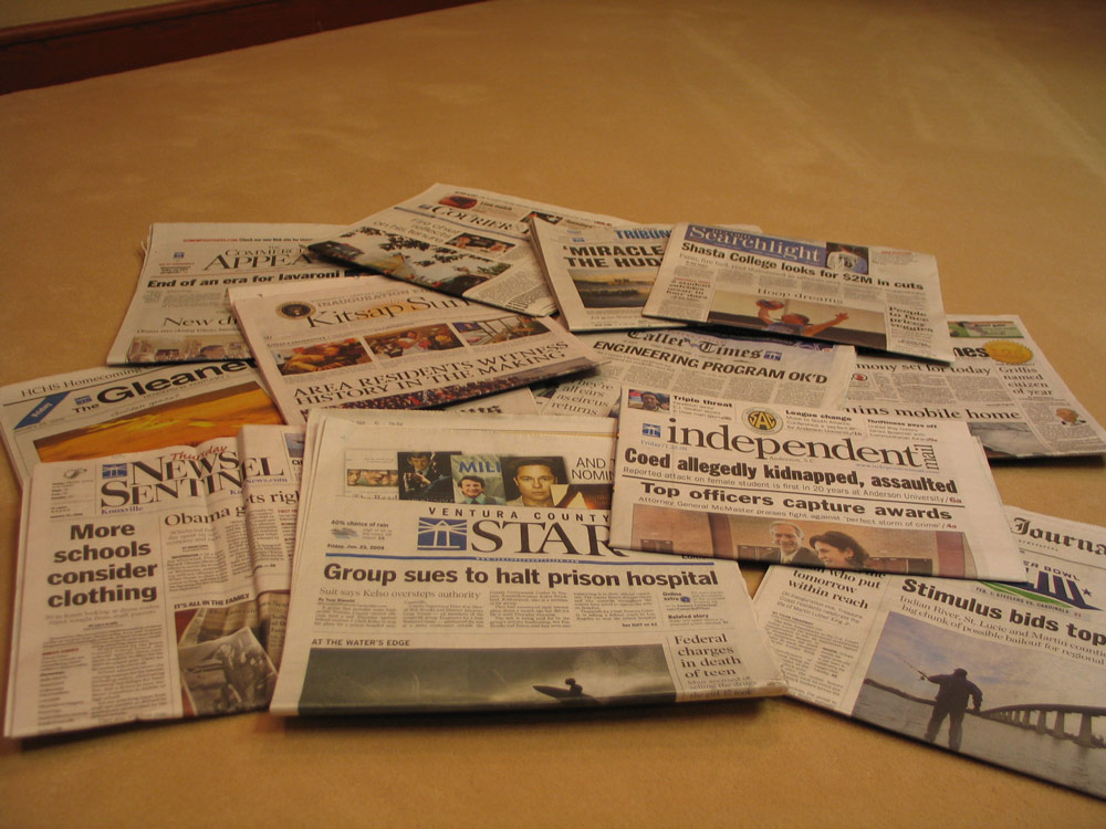 Photo of multiple newspapers scattered all over a brown, wooden table